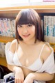 A woman sitting in front of a bookshelf wearing a white bra.