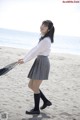 A woman in a school uniform holding an umbrella on the beach.